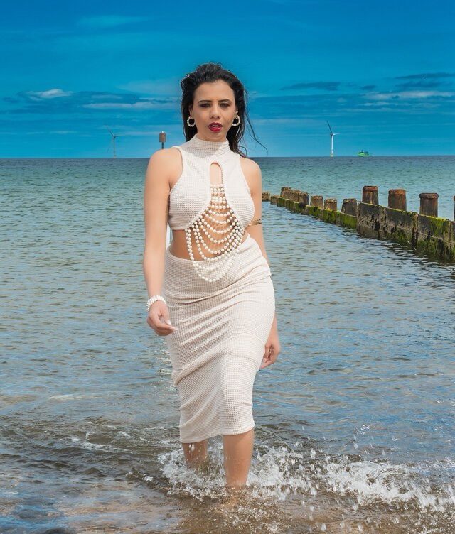 Natasha walking in the sea in a white pearl dress